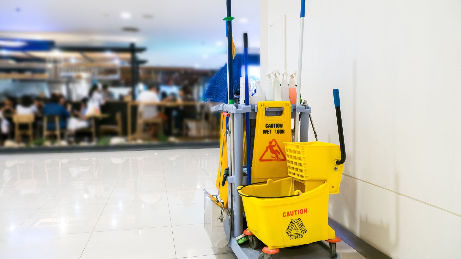 Yellow janitorial cart with mop, bucket, and wet floor caution sign